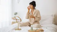A person sitting on their bed with a tray of skincare and a mirror in front of them.