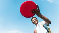 A child flings a red frisbee outside.