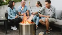 Group of people sitting around the Solo Stove Bonfire fire pit roasting marshmellows