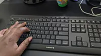 A person's hand touching a black keyboard