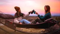 Two friends sitting on their camping hammock during a trip.