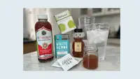 Kombucha, matcha, yerba mate, green tea, honey, cider vinegar, and a large glass of water on a marble counter.