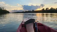 POV from seat of pedal kayak on a Missouri lake at dusk. Trees line the horizon.