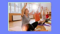 Seniors sitting cross-legged on yoga mats with arms raised in the air during a guided yoga fitness class.