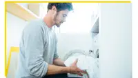 A person taking white sheets out of a drying machine.