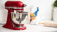 A red KitchenAid stand mixer on a countertop with baking accessories.