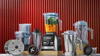 Several Vitamix blenders and accessories in front of a red backdrop