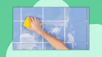 A hand wearing a glove washes a tiled wall with a sponge.