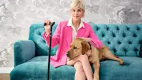 Selma Blair, QVC Brand Ambassador For Accessibility, Sits On A Plush Teal Sofa With Her Dog, Scout. She Wears A Hot Pink Suit And Uses A Black And Gold Cane.