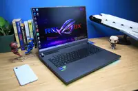 An open and powered on laptop sitting on top of a desk flanked by various objects