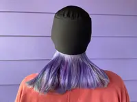 A person wearing the AllSett Health Migraine Relief Cap on a purple background.