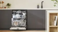 Open Bosch dishwasher, revealing three racks full of dishware, in a modern kitchen