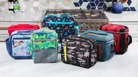 Eight colorful lunch coolers from brands like L.L. Bean, PackIt, Pottery Barn Kids, and Coleman sit on a kitchen counter.