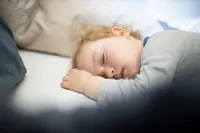 A blonde toddler sleeping in a bed with a pillow.