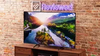 The Hisense U6K displaying a colorful 4K image of a river and a sunset while it sits in front of a brick wall in a living room setting