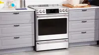 The Café CHS900P2MS range between two sets of grey cabinet drawers in a kitchen.