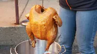 Fried turkey hanging above a pot outdoors