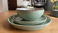A stack of teal dinnerware with orange rims. The stack has one dinner plate, one salad plate, and a cereal bowl.