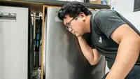 A person crouched down and listening closely to a dishwasher.