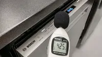 A decibel meter held in front of a dishwasher with a 42.5 reading on the screen.