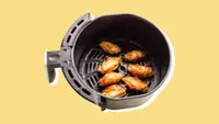 A batch of chicken wings in an air fryer basket, on a yellow background