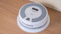 A round, white smoke detector sits on a wood background