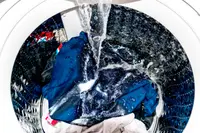 A washing machine being filled with water, with some clothing and powder detergent inside