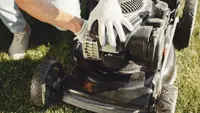 Person replacing blade on lawn mower while wearing gloves.