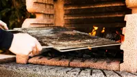 A person's hand holding baking metal sheet from outdoor barbecue