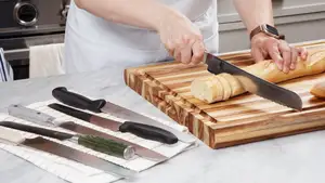 Hand cutting a baguette with a serrated bread knife, beside several other bread knives
