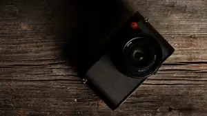 A black Leica Q (Typ 116) camera sits on a wooden table facing up