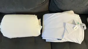 White Cooloxy Breathable Cooling Comforter and SleepEase Cooling Comforter Set next to each other on a dark grey couch.