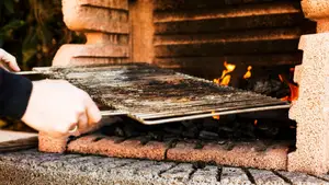 A person's hand holding baking metal sheet from outdoor barbecue