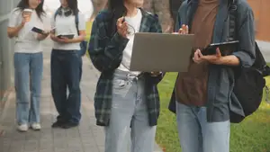 A group of students on the sidewalk holding notebooks, a laptop and an iPad