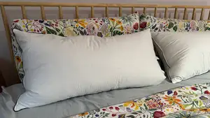 Two white Pacific Coast Feather & Down Pillows on a bed with floral sheets and a wooden barred headboard.