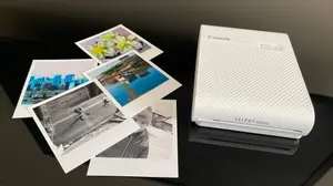 The Canon Selphy portable photo printer on a table next to some photographs.