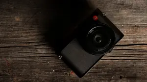 A black Leica Q (Typ 116) camera sits on a wooden table facing up