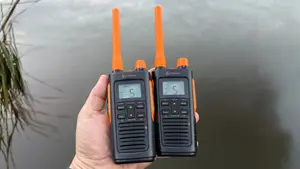 Two Cobra walkie-talkies held in hand with a lake in the background