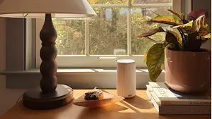 Pura diffuser review setup featuring a compact white Pura smart fragrance diffuser on a windowsill beside a lamp, books, and houseplant in a sunlit room.