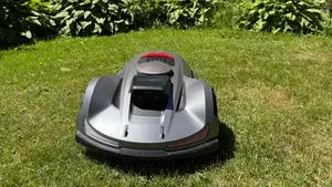 Silver Sunseeker Elite X7 robot lawn mower on grass in front of some bushes.