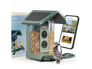 Four bird feeders in blue and green shades sit in a group on a brown table with a garden and green grass in the background