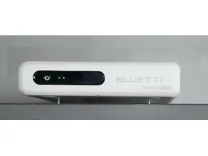 Bluetti FridgePower shown on top of a silver refrigerator in front of wooden cabinets, with a disco ball hanging from the ceiling in the basement shown in the background.