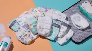 A stack of baby's diapers in the middle a changing mat and baby wipes and a pile of talcum powder.