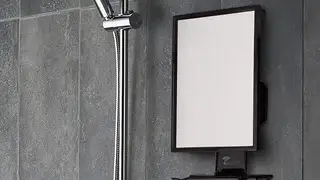 A fogless shower mirror being used for music and for a man to shave.