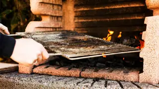 A person's hand holding baking metal sheet from outdoor barbecue