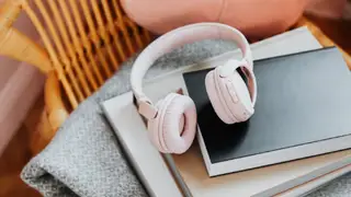 A pair of pink over-the-ear headphones sits on a stack of books