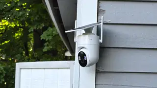 White Elysoo 4K Wifi Solar Camera mounted on a grey house with trees in the background.