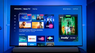 Philips Ambilight 7985 TV displaying Roku streaming options with blue illuminated light behind it.