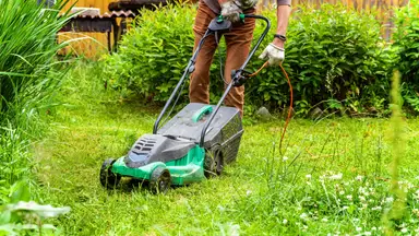A person pushing a lawnmower mowing a lawn