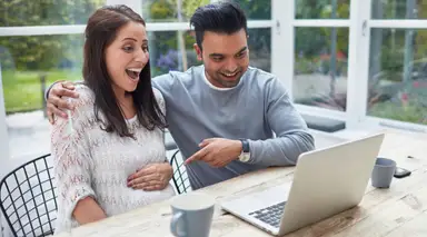 A pregnant woman and man sitting at an outdoor patio table using the computre